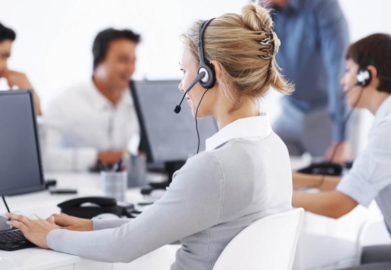 An image of a customer service representative at a desk wearing a headset and talking on the phone.